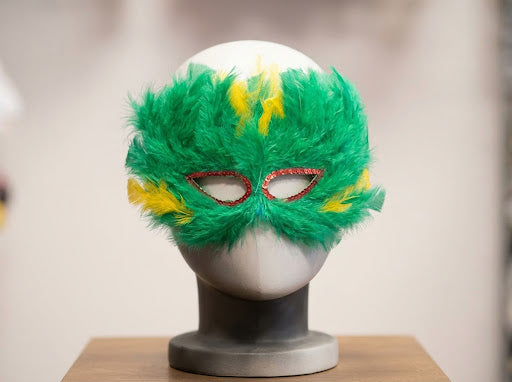 Antifaz de plumas verdes con detalles amarillos y ribete rojizo alrededor de los ojos
