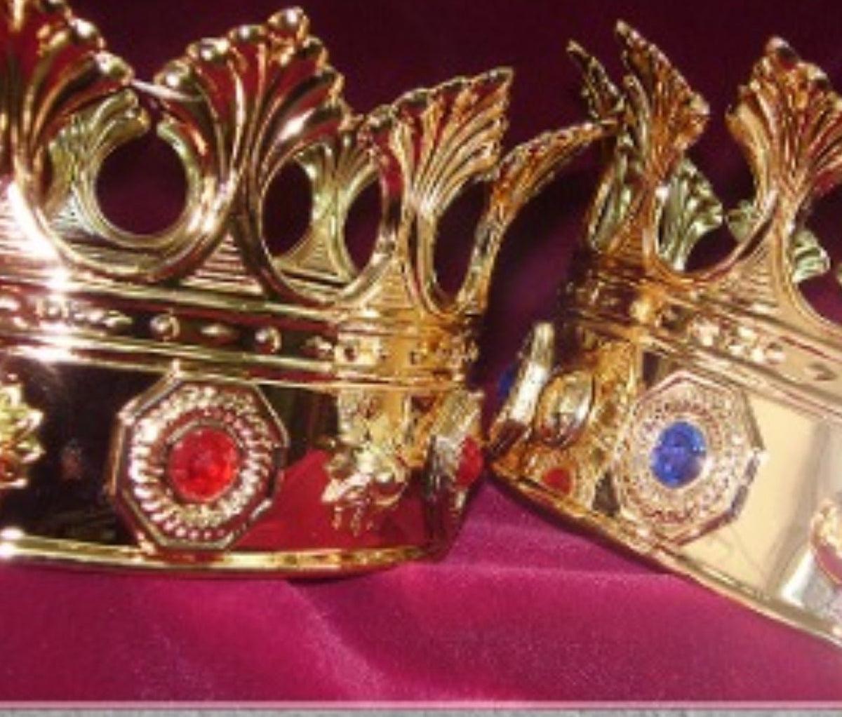 Corona real dorada con gemas roja y azul y puntas altas sobre tela morada