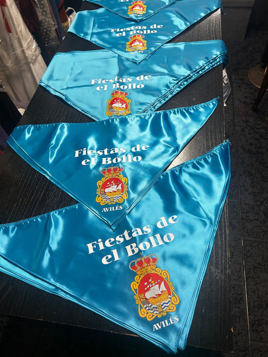Pañuelos satinado azul apilados con escudos y texto “Fiestas de el Bollo”