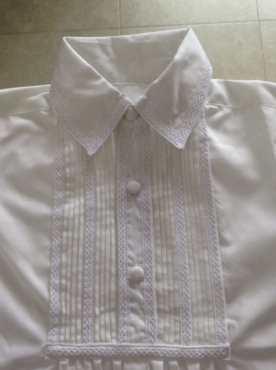 Camisa blanca con cuello bordado, botones frontales y franjas verticales con encaje.
