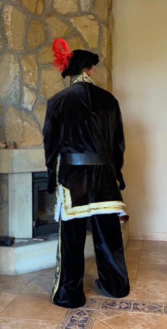 Traje de rey Gaspar negro con capa trasera y cenefa dorada; sombrero con penacho rojo